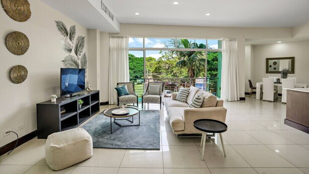 A modern living room with a sofa, coffee table, and TV, large windows with a view of greenery, and a balcony. - PP201: Modern Space in Centre of Town (Tamarindo)