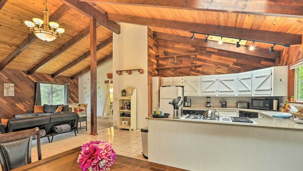 A spacious kitchen with white cabinets and a central island, a dining area with a wooden table and chairs, and a living room with a dark sofa and a chandelier. - Step-Free Hawkins Bar Home Near Trinity River (Salyer)