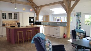 A spacious kitchen with a central island, wooden stools, and a dining area with a table and chairs. - The Anchorage @ Nables Farm (Chippenham)