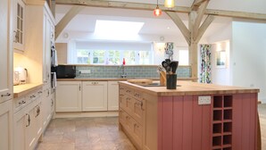 A modern kitchen with white cabinetry, a wooden island, and a large window providing natural light. - The Anchorage @ Nables Farm (Chippenham)