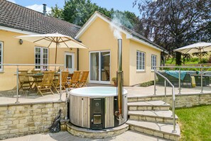 A hot tub in front of a house with a patio area, outdoor furniture, and a stone wall. - The Anchorage @ Nables Farm (Chippenham)