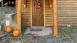 Una cabaña de madera con un porche, una puerta principal adornada con un adorno y dos calabazas en primer plano.