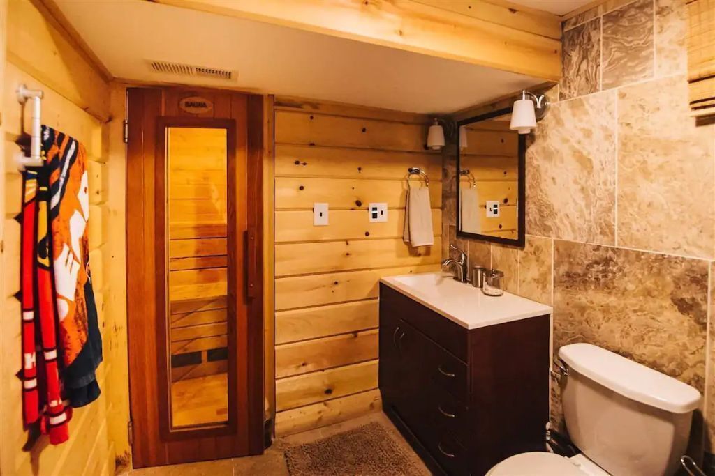 A wooden cabin bathroom with a wooden door, a sink, a mirror, and a toilet.