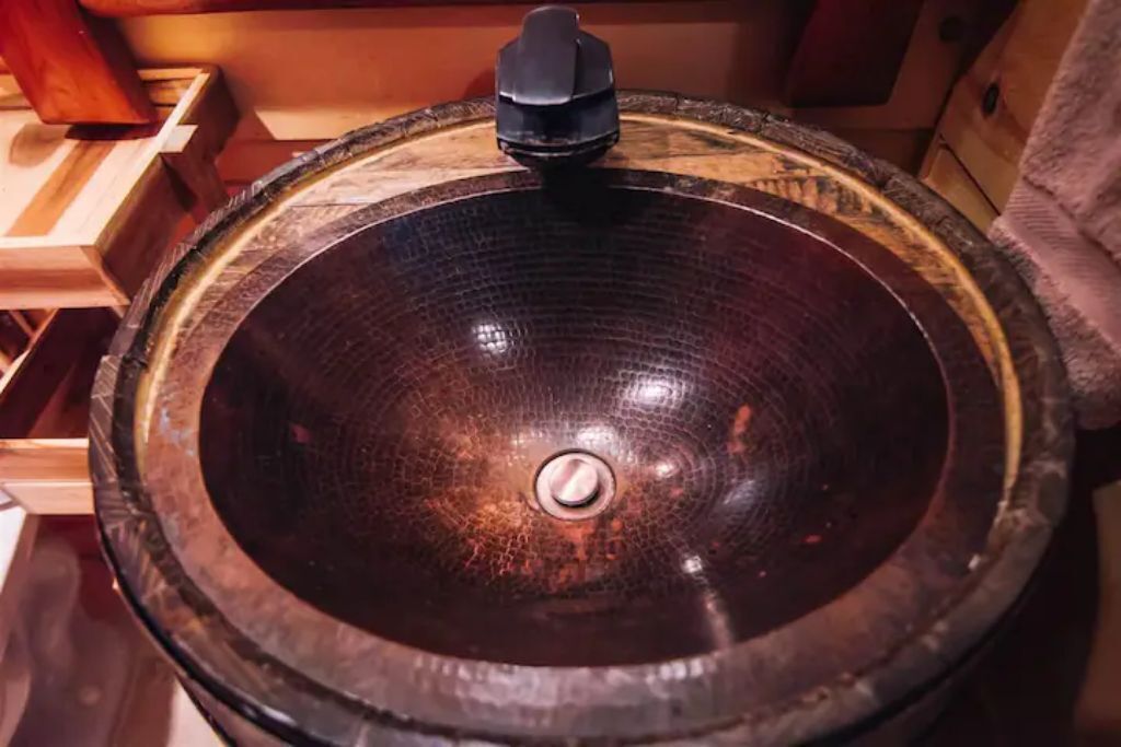 A round, dark wooden bowl with a central spout, likely used for water or other liquids.
