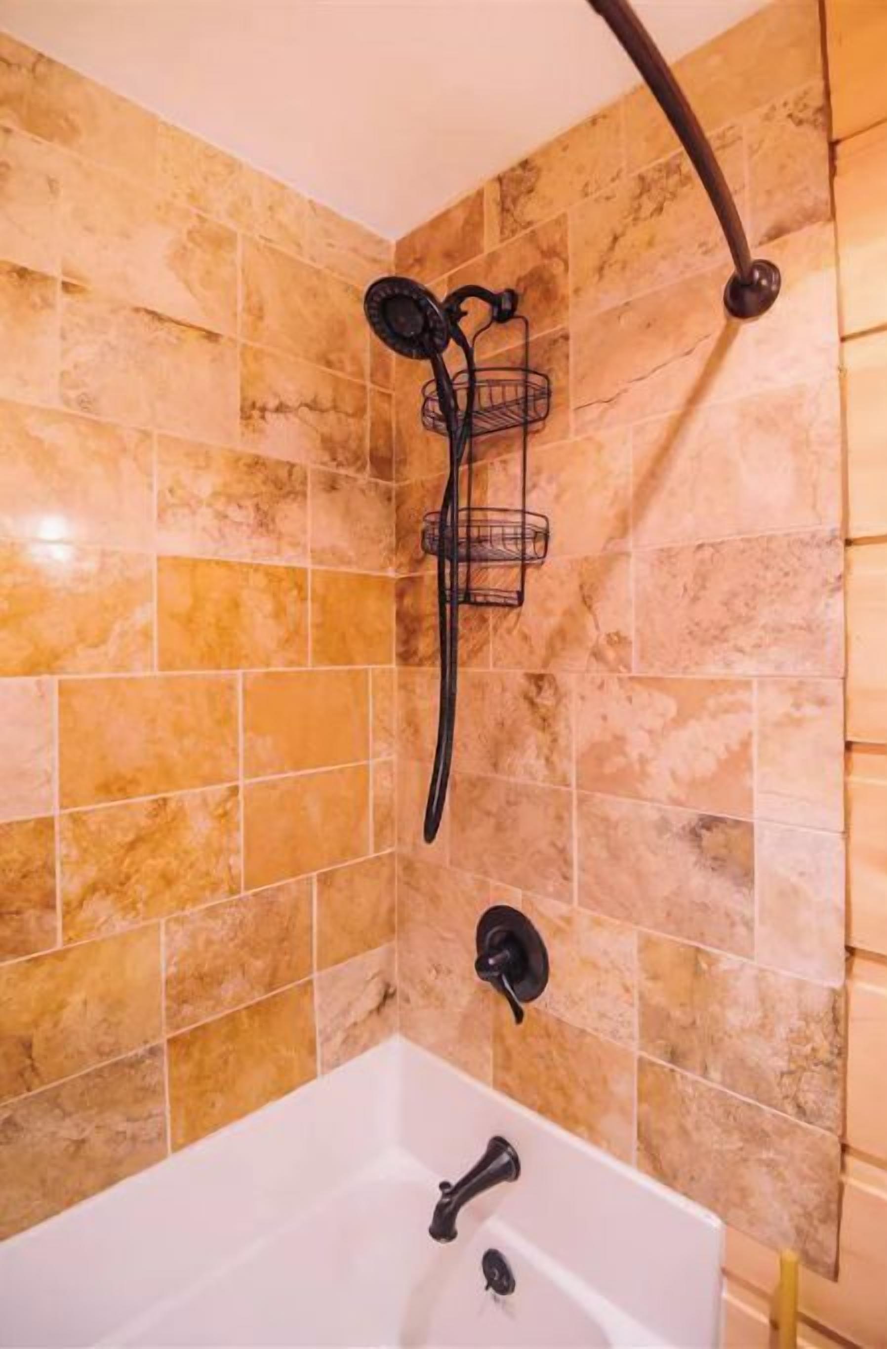 A bathroom with a bathtub, a shower with a black hose, and a wall-mounted towel rack.