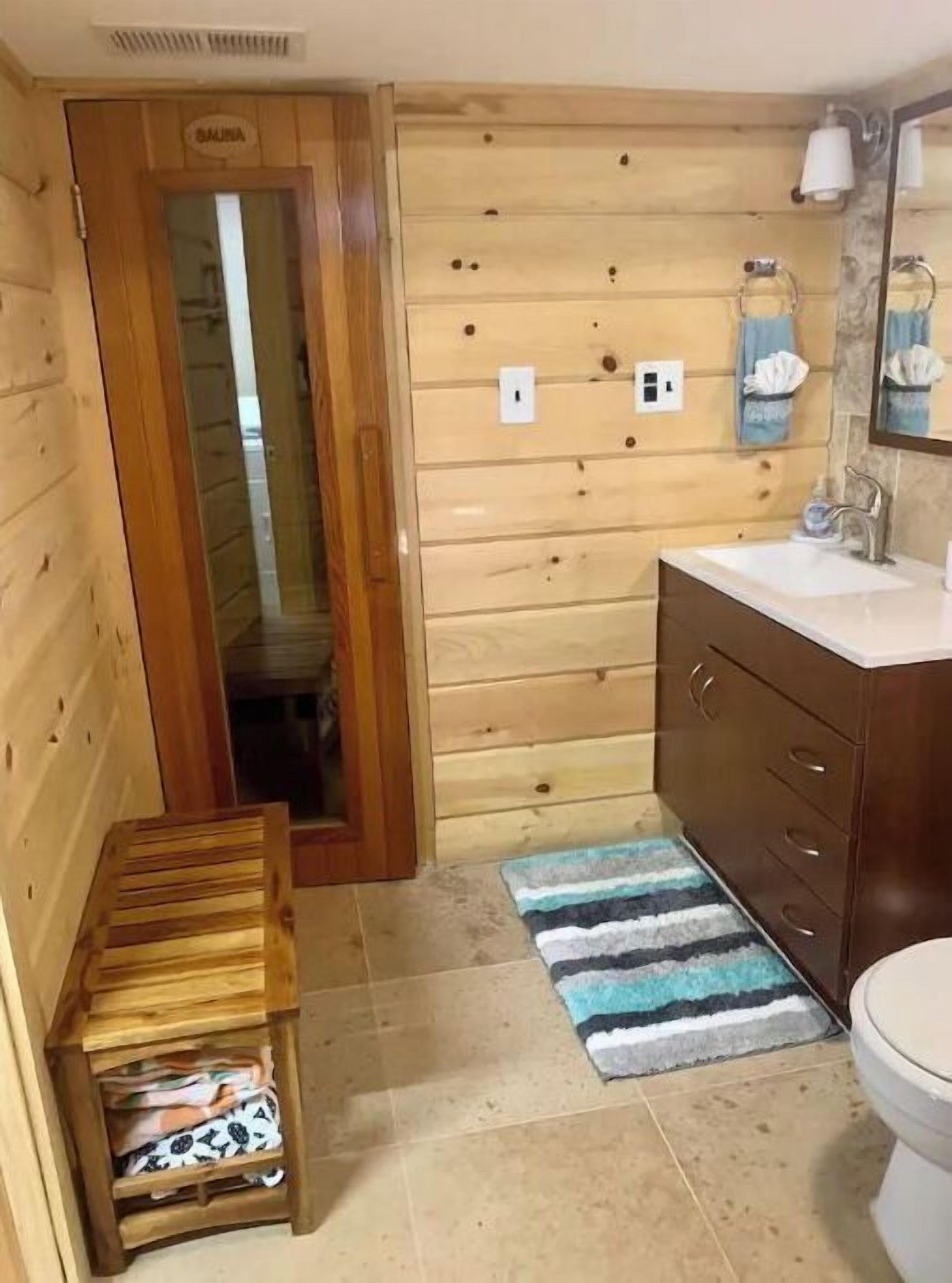 Un baño con paneles de madera, un banco de madera, un lavamanos y un inodoro.
