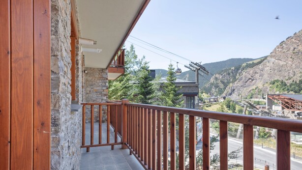 A balcony with a stone wall and wooden railing overlooking a mountainous area with a road and a cable car. - Luderna - Apartamento D2 Suriguera de Canillo (Canillo)