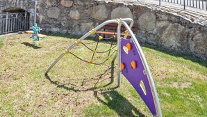 A stone building with multiple balconies, a playground, and a stone wall. - Luderna - Apartamento D2 Suriguera de Canillo (Canillo)