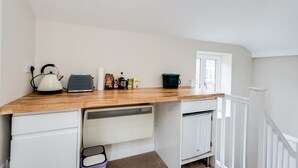 Cocina compacta con encimera de madera, armarios blancos, hervidor, tostadora y ventana que proporciona luz natural.