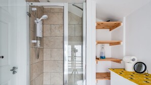 Un baño moderno con cabina de ducha de vidrio, inodoro blanco y estantes de madera con artículos de aseo.