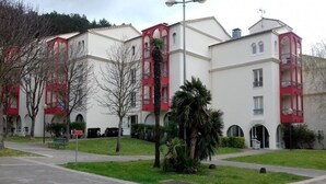 Una hilera de edificios blancos con detalles rojos y balcones, rodeada de césped verde y árboles.