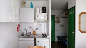 Cocina compacta con microondas, cafetera y refrigerador pequeño. En primer plano, una mesa de comedor con mantel estampado.