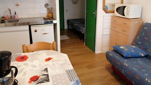 Una habitación compacta con kitchenette, un comedor con mesa y sillas, una cama con cubrecama estampado y un microondas.