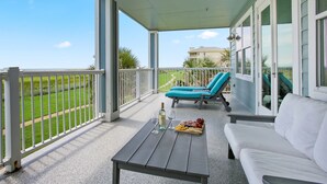 Een overdekt balkon met een witte reling, een tafel met een fles en glazen, en twee blauwe loungestoelen.