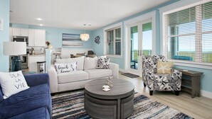 Een woonkamer met een bank, fauteuil, salontafel en uitzicht op de keuken en eetruimte.