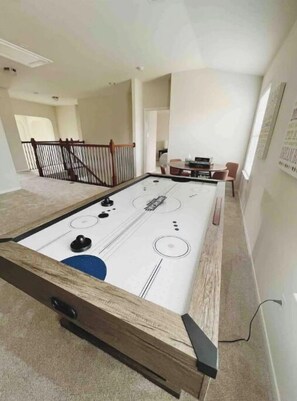 A pool table in a spacious room with a high ceiling and a staircase in the background.