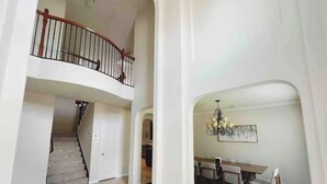 A spacious interior with a staircase leading to a second floor, a dining area with a chandelier, and a hallway with a door. - Spacious | Large Groups | Katy Mall, Parks! (Katy)