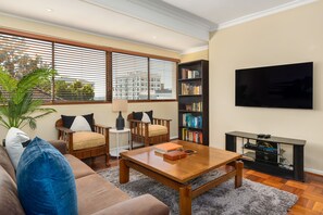 A living room with a sofa, coffee table, bookshelf, and a TV. - Middelhof 23 (Cape Town)