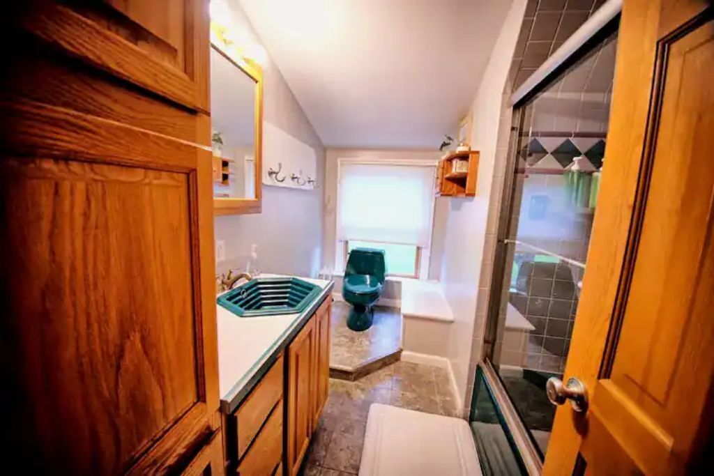 Een kleine badkamer met een houten wastafel, een raam en een douchehoek.