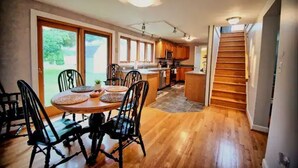 Un comedor con una mesa y sillas de madera, una cocina al fondo y una escalera que sube a otro nivel.