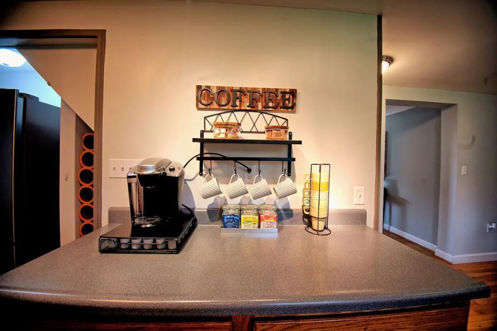 A kitchen counter with a coffee maker, a shelf with coffee mugs, and a coffee-themed wall decoration.