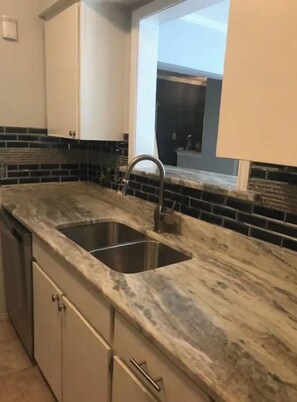 A kitchen with a double sink, a dishwasher, and a window above the sink.