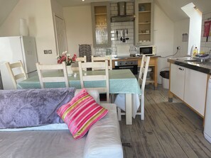 Un salon confortable avec un canapé et des fauteuils, une table à manger avec des chaises, un coin cuisine équipé d’un four à micro-ondes, d’une cuisinière et de placards.