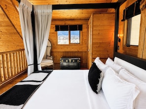 A wooden cabin bedroom with a bed, a chair, a suitcase, and a window with a view.