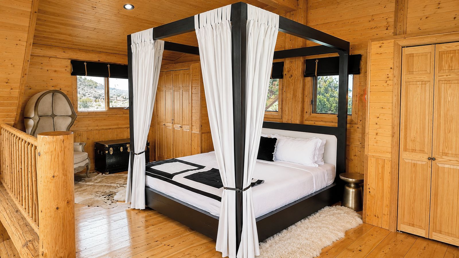 A four-poster canopy bed in a wooden cabin room with a view of the outdoors.