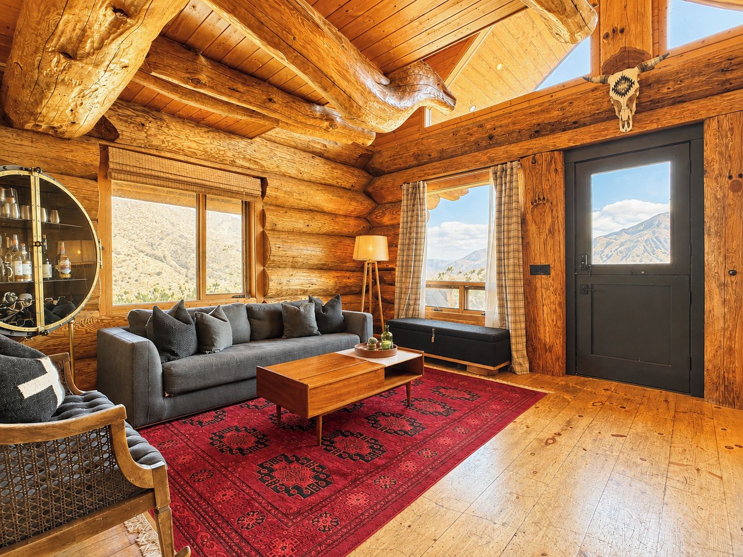 L’intérieur d’une cabane en rondins, avec un canapé, une table basse et une grande fenêtre donnant sur une vue imprenable sur les montagnes.