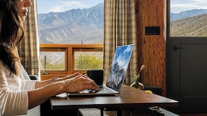 A person using a laptop at a wooden table with a mountain view through a window.
