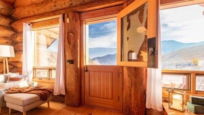 Ein gemütliches Blockhaus-Interieur mit Holzwänden, einer gepolsterten Sitzecke und großen Fenstern mit Blick auf die Berge.
