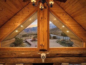 A wooden interior with a view of a desert landscape and a bridge.