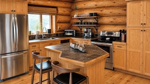 A kitchen with a stainless steel refrigerator, a built-in oven, a coffee maker, and wooden cabinets.
