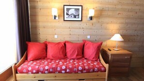 Ein Holzbett mit Etagen, ausgestattet mit roter Bettwäsche, zwei Wandleuchten, einem gerahmten Bild und einem Nachttisch mit Lampe.