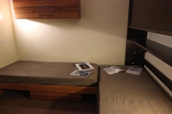 A small, single-bed room with a wooden headboard and a shelf above the bed.