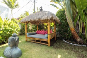 A thatched-roof outdoor seating area with cushions and a decorative stone sculpture.