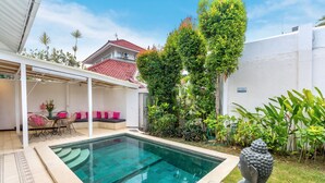 Una piscina con un'area relax coperta, circondata da vegetazione e una statua di Buddha.