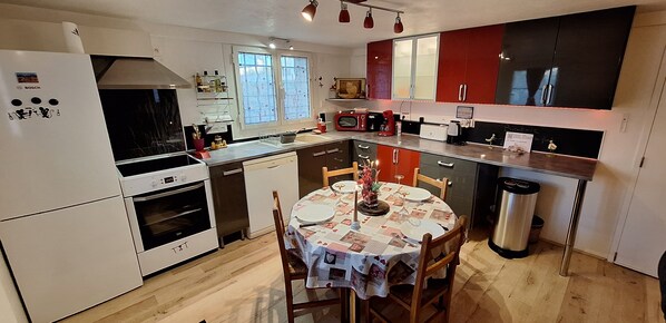 A modern kitchen with white appliances, a dining table set for four, and red cabinets.
