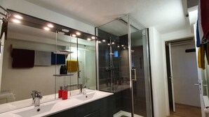 Een moderne badkamer met een grote spiegel, twee wastafels en een douche met glazen wanden.