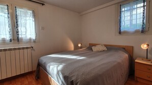 Een slaapkamer met een bed, nachtlampjes, een radiator en ramen met gordijnen.