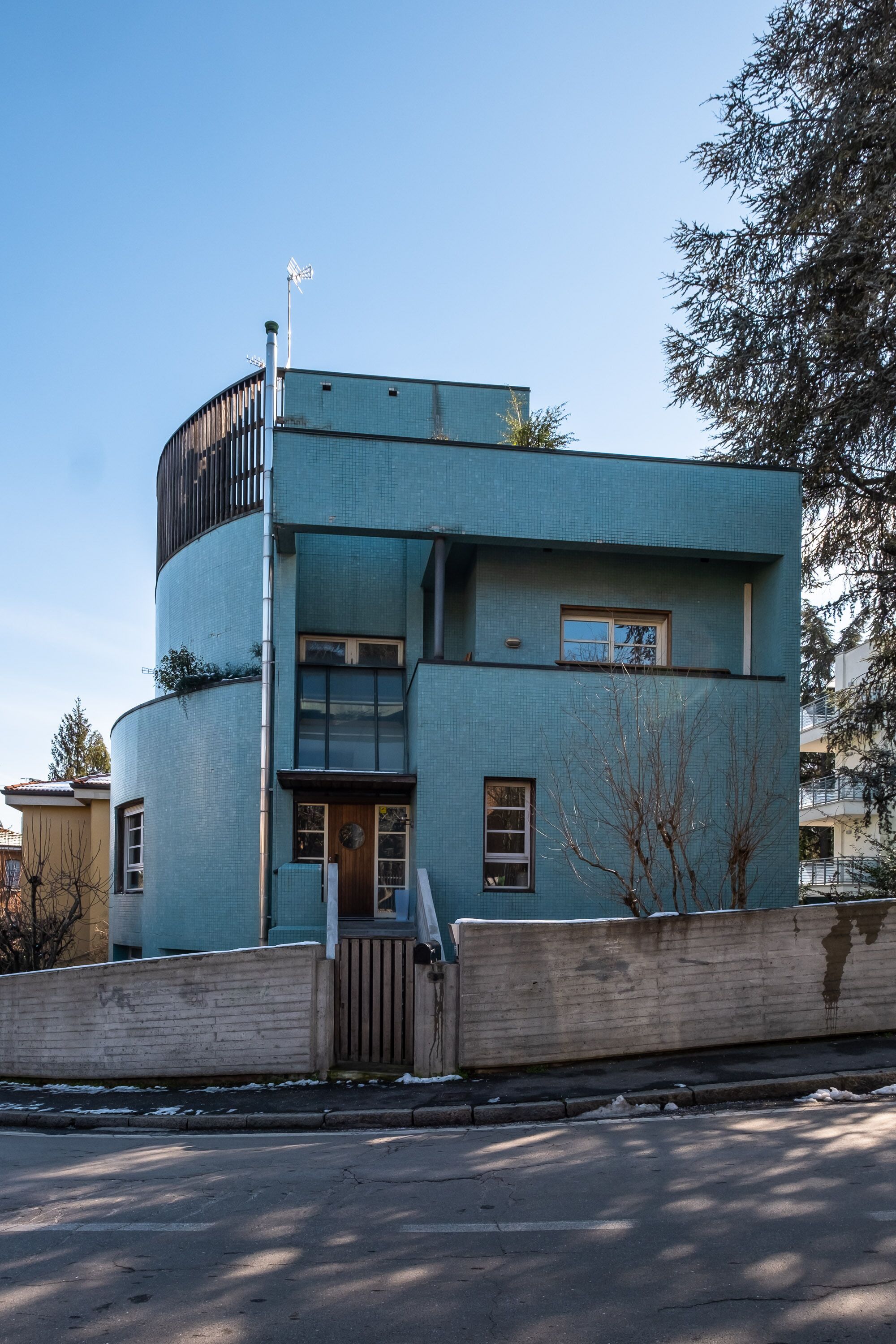 A modern, multi-story building with a curved facade, large windows, and a small balcony.