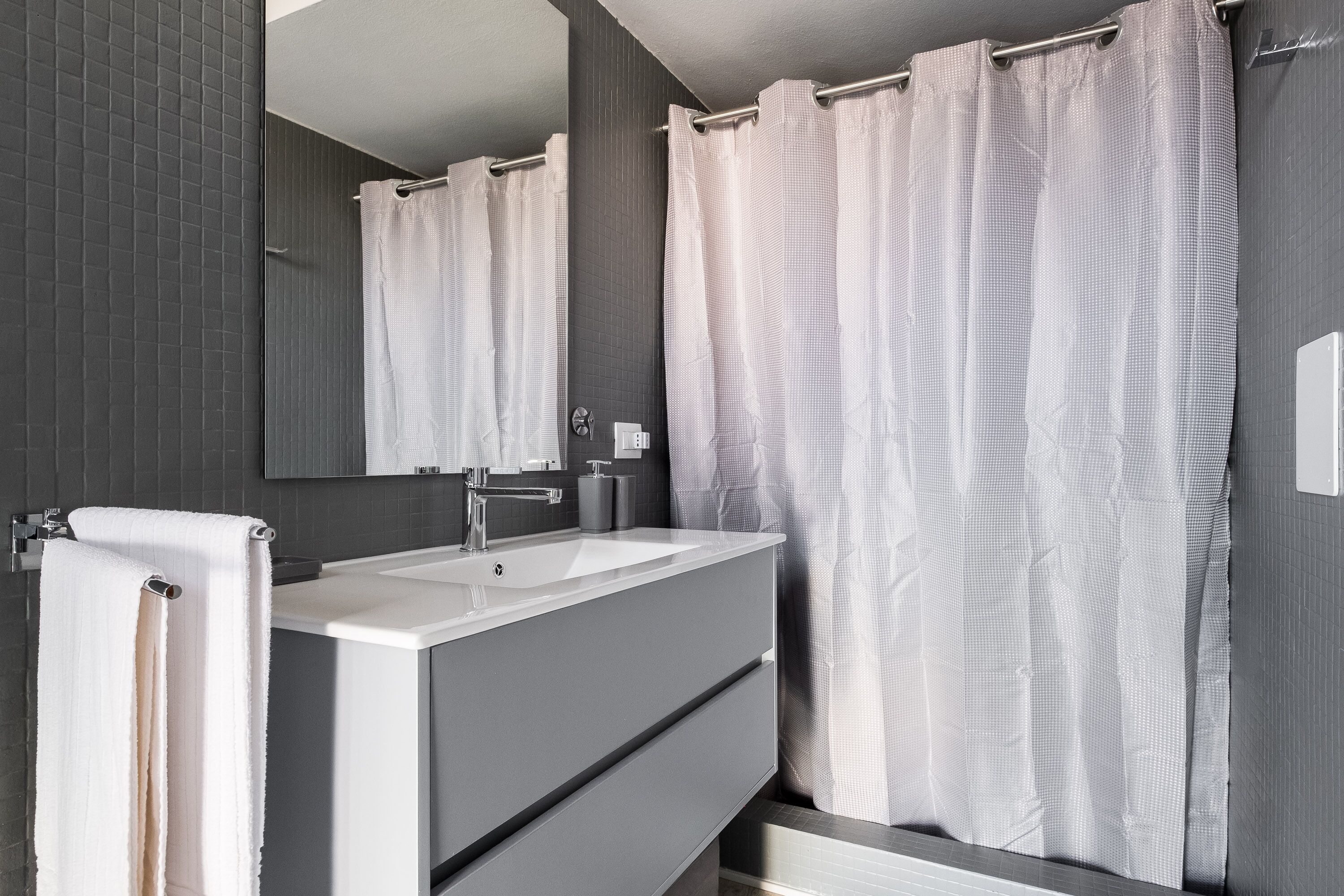 A modern bathroom with a large mirror, white sink, and a shower curtain.