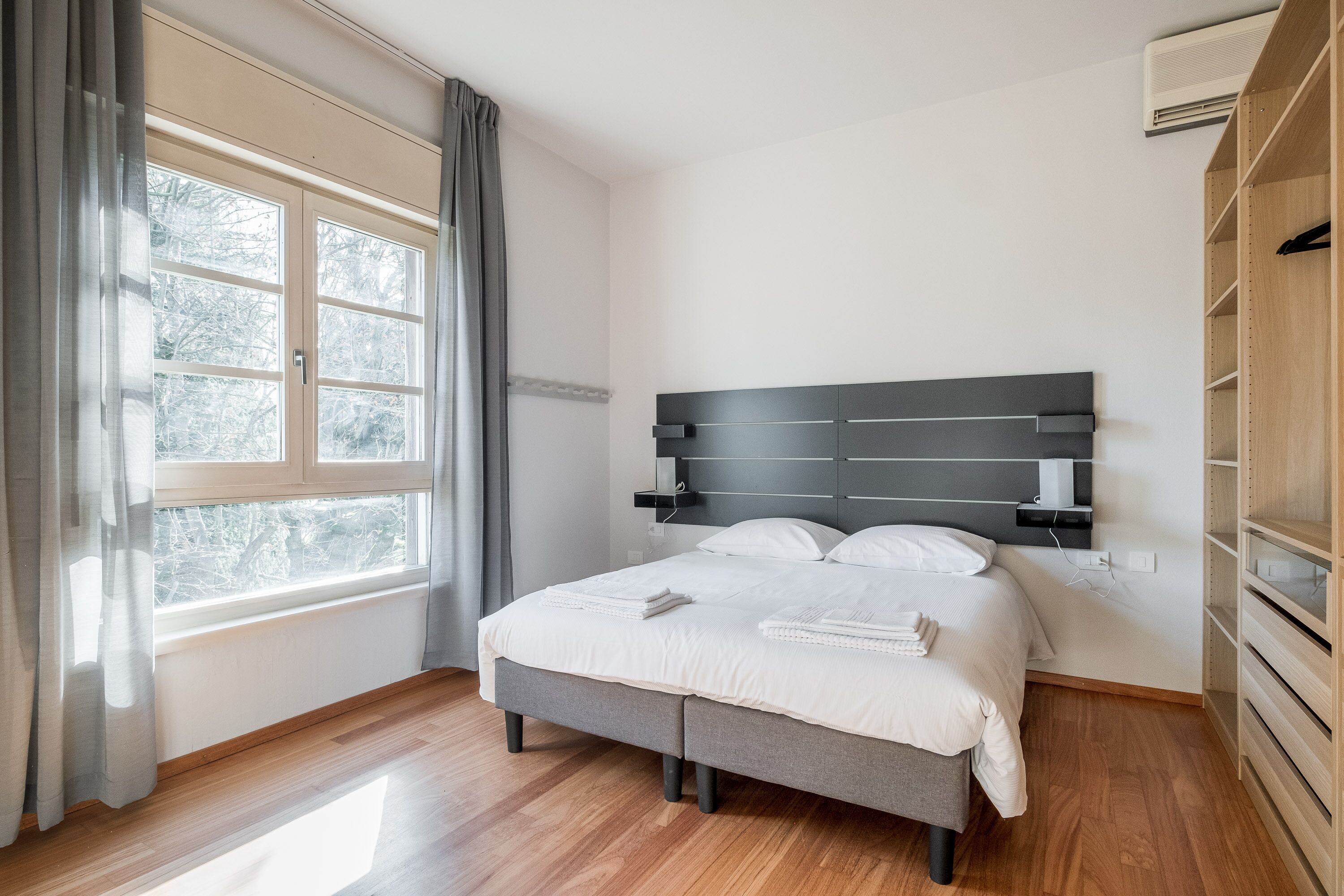 Un dormitorio con cama, ventana con cortinas, mesita de noche y armario.