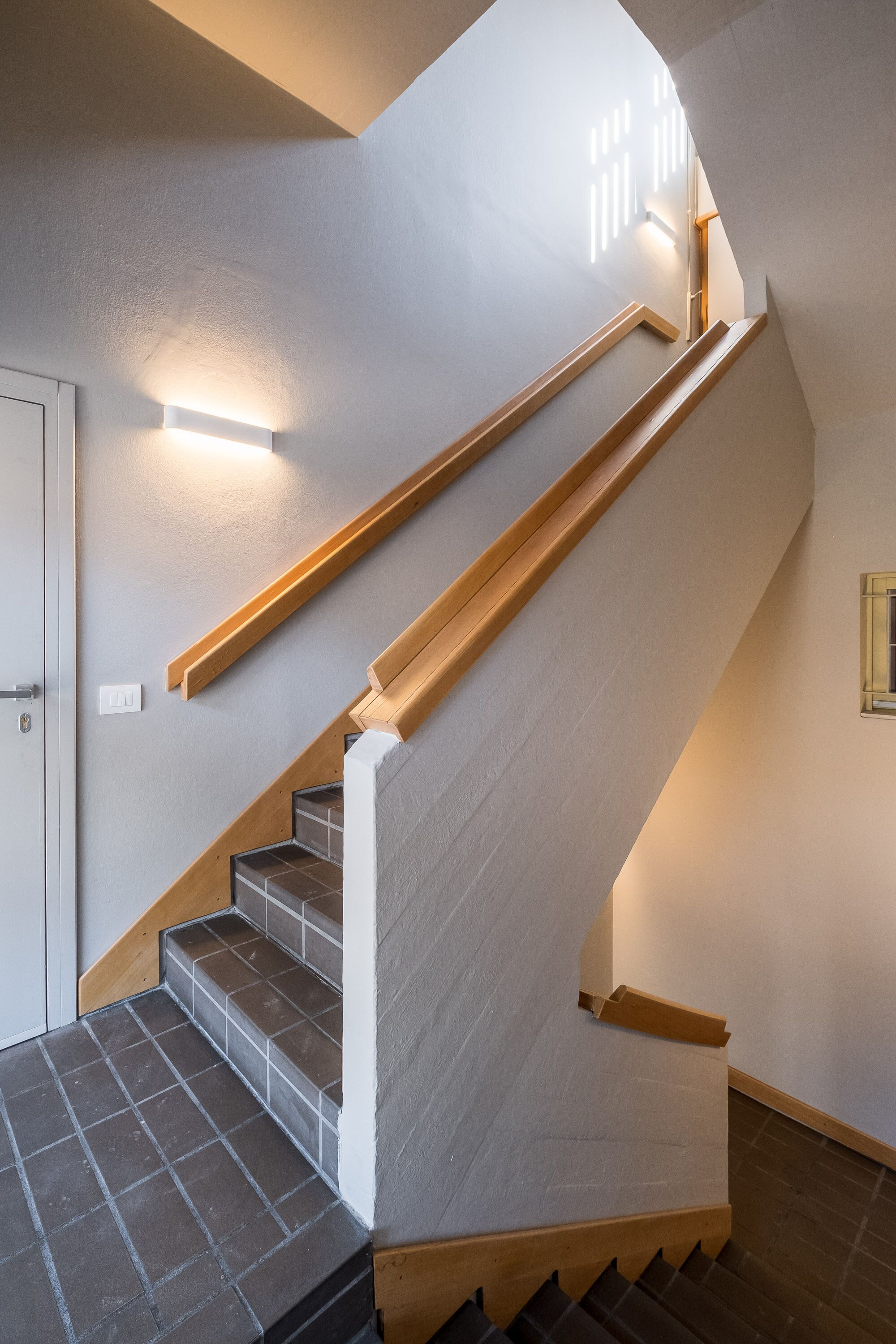 Een trap met houten leuningen en een lamp aan de muur.