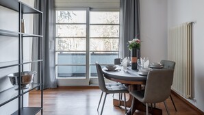 Un comedor con una mesa dispuesta para cuatro, una estantería y un ventanal con cortinas.