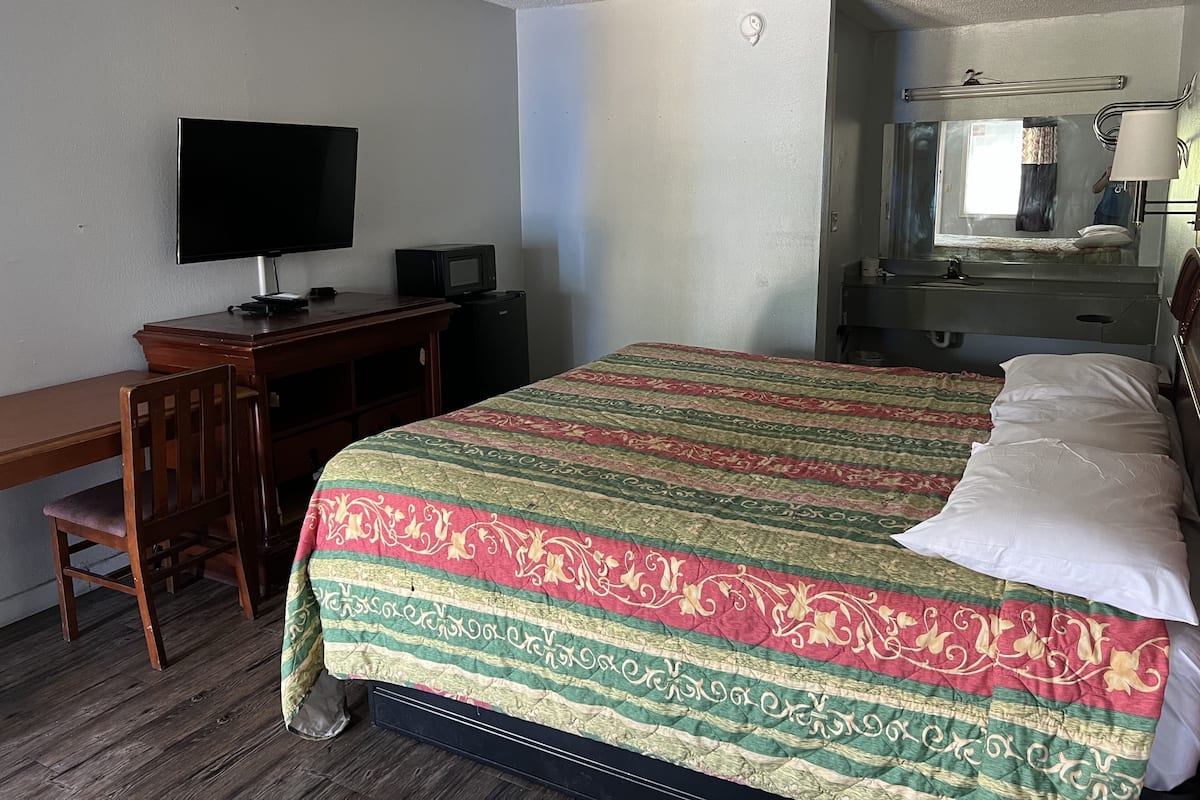 A hotel room with a bed, a desk with a television, a small refrigerator, and a window with a curtain.