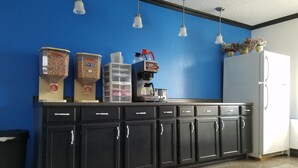 Ett kök med en blå vägg, svarta skåp och ett vitt kylskåp. På bänkskivan står tre behållare och en kaffemaskin.