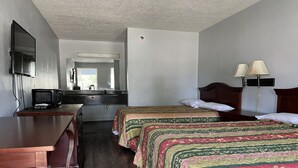 Ett hotellrum med ett skrivbord i trä, två sängar med mönstrat sänglinne, en tv och ett fönster.