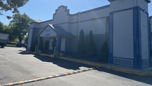 En byggnad i västerländsk stil, inredd som ett värdshus, med en blå och vit fasad, en överbyggd entré och en parkeringsplats.